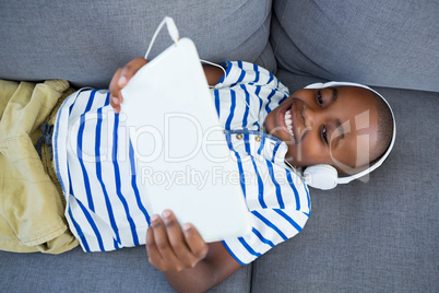 High angle view of boy using digital tablet while listening to headphones on sofa at home