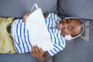 High angle view of boy using digital tablet while listening to headphones on sofa at home