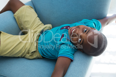 High angle portrait of boy lying on blue armchair at home