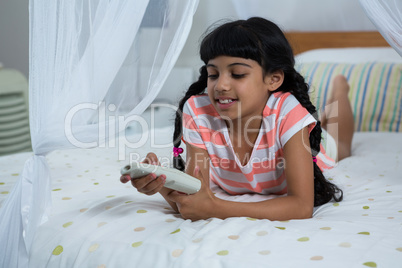 Girl pressing remote control while lying on bed