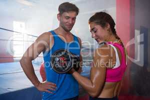 Smiling male looking at female athlete lifting dumbbell