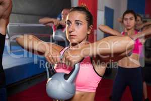 Young woman exercising with kettle against athletes