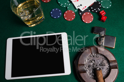 Ashtray, lighter, digital tablet, dice, casino chips and playing cards on poker table