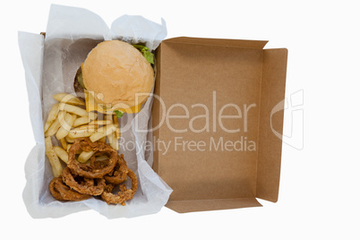 Hamburger, onion ring and french fries in a take away container on table