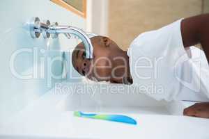 Side view of boy washing mouth from faucet