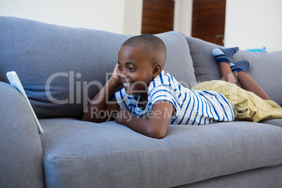 Smiling boy looking at mobile phone while lying on gray sofa