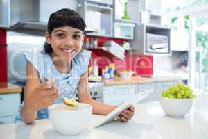 Portrait of girl eating breakfast with digital tablet in kitchen