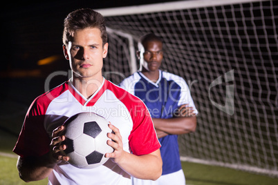 Portrait of confident soccer player holding ball with rival athlete