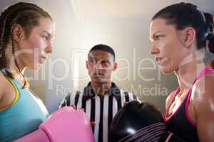 Female boxers looking at each other against referee