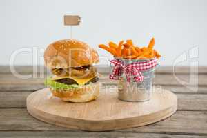 Hamburger by french fries in container on cutting board