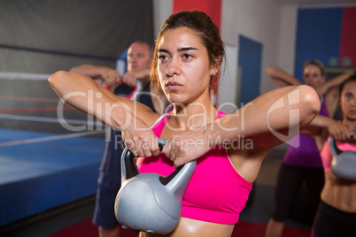Young woman lifting kettle against athletes