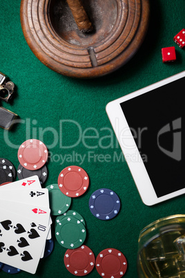 Ashtray, digital tablet, dice, casino chips and playing cards on poker table