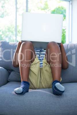 Boy sitting on sofa while using laptop against window Boy sitting on sofa while using laptop against window