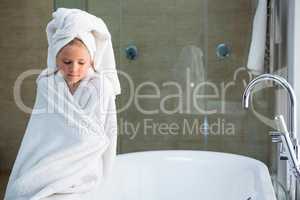Sad girl wrapped in towel sitting on bathtub
