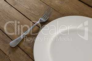 White plate and fork on wooden table