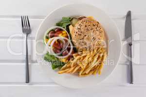 Hamburger, french fries, and salad in plate on wooden table