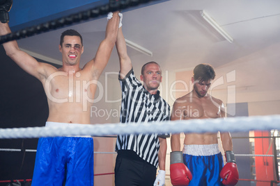 Referee holding hands of smiling male boxing winner by athlete