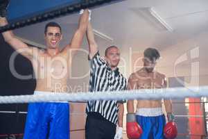 Referee holding hands of smiling male boxing winner by athlete