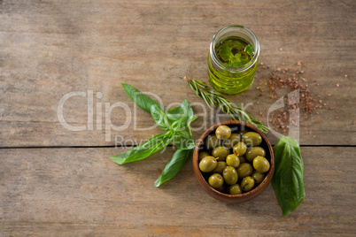 Marinated green olives in bowl and oil container with green leaf on table