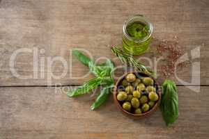 Marinated green olives in bowl and oil container with green leaf on table