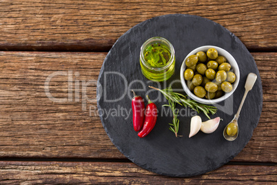 Green olives, fresh herbs with olive oil and red chilies on table