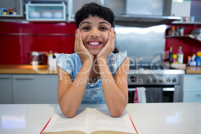Portrait of smiling girl sitting with novel in kitchen