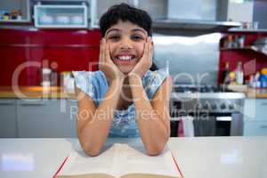 Portrait of smiling girl sitting with novel in kitchen