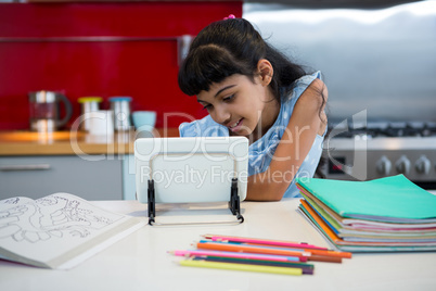 Girl using digital tablet amidst colored pencils and books