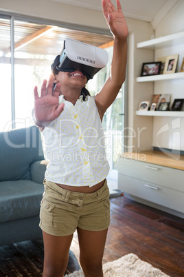 Girl using virtual reality simulator while standing in living room