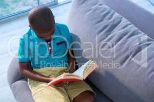 High angle view of boy reading novel on sofa at home