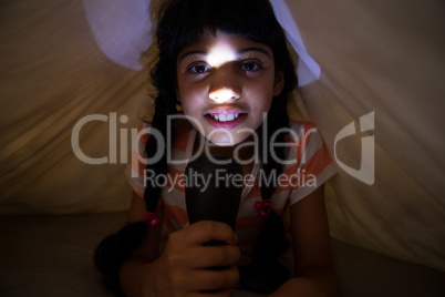 Close-up portrait of girl holding illuminated flashlight under blanket