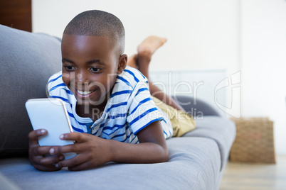 Smiling boy using mobile phone while lying on sofa at home