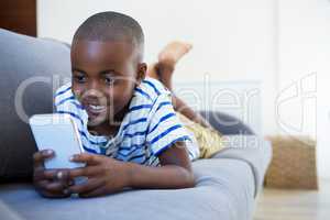 Smiling boy using mobile phone while lying on sofa at home