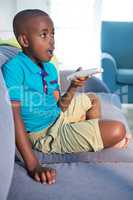 Surprised boy holding remote control while sitting on sofa at home