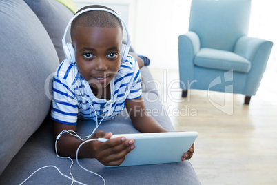 High angle portrait of boy using digital tablet while listening to headphones on sofa at home