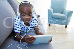 High angle portrait of boy using digital tablet while listening to headphones on sofa at home