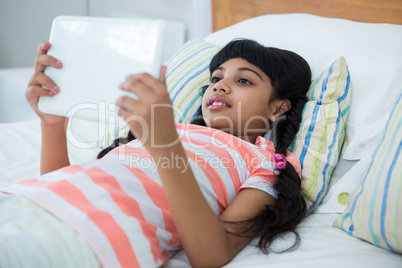 Girl using tablet computer while lying on bed at home