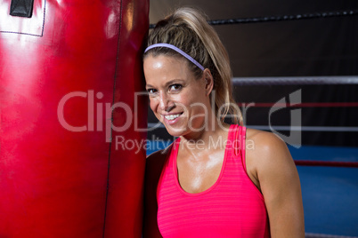 Portrait of smiling young female athlete leaning on red punching bag