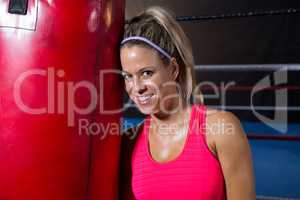 Portrait of smiling young female athlete leaning on red punching bag