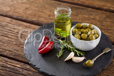 Green olives, fresh herbs with olive oil and red chilies on table