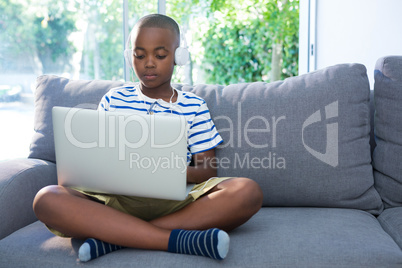Boy using laptop while listening to headphones at home