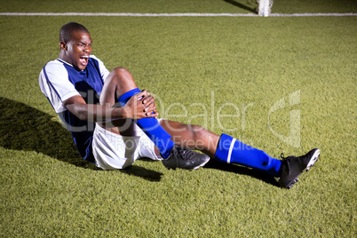 Young male soccer player shouting in agony with knee pain