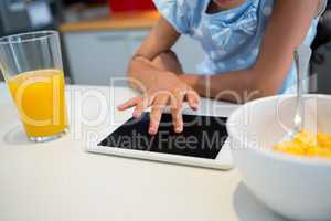 Midsection of girl using digital tablet by breakfast on kitchen counter