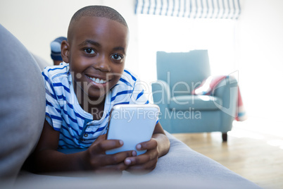 Portrait of smiling boy holding mobile phone lying on sofa at home