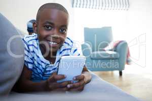 Portrait of smiling boy holding mobile phone lying on sofa at home