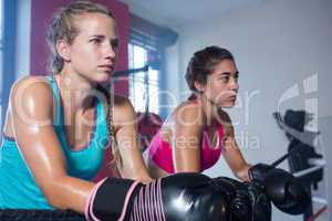 Young female boxers leaning on rope while looking away