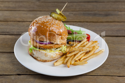 Hamburger, french fries and salad in plate on wooden table