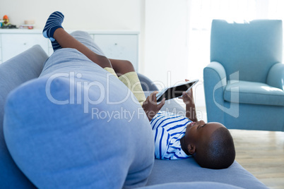 Boy using tablet computer while lying by cushion on sofa at home
