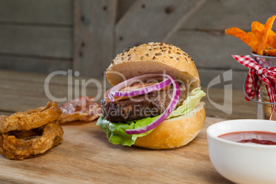 Hamburger, french fries, onion ring and tomato sauce on chopping board