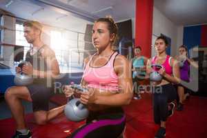 Group of young athletes practicing lunge exercise with kettles